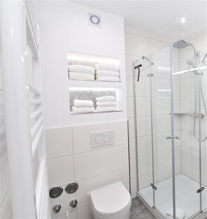 A modern bathroom with a glass-enclosed shower, a toilet, and a towel rack. - Glücks-Burg "Stars" vacation apartment (Glücksburg)