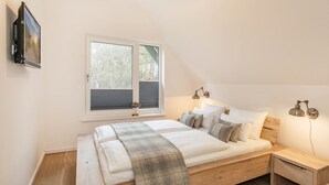 Un dormitorio con cama, ventana, mesita de noche y lámpara de pared.