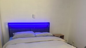A bed with a headboard, a bedside table, and a power outlet on the wall. - Room-cozy Room Near Airport (Perth)