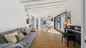 A modern living room with a grey sofa, a dining table, and a piano.