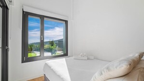 A bedroom with a bed, a window with a view of greenery, and a towel on the bed.