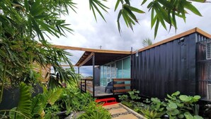 Um espaço ao ar livre moderno com estrutura de vidro, deck de madeira e diversas plantas.