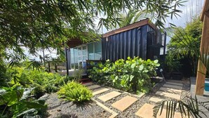 Um jardim com um caminho de pedra, diversas plantas e um edifício moderno com grandes janelas.