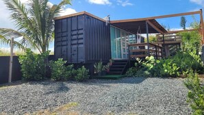 Uma casa moderna com uma grande estrutura em forma de contêiner, um deck de madeira e uma escadaria para uma área coberta.