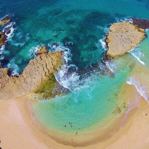 An aerial view of a beach with clear turquoise waters, rocky formations, and a sandy shoreline. - House VillaCecilia. Sea view. Pool with heater (Islote)