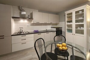 A modern kitchen with white cabinets, a gas stove, a stainless steel range hood, a glass dining table with chairs, and a built-in cabinet with glass doors. - Just a short walk from Marzocca Beach, Casa Neroli is an elegant and welcoming holiday home designed for guests seeking relaxation, comfort, and authentic Mediterranean living.Perfect for 3–4 guests, the house features two stylish bedrooms, two modern  (Marzocca)