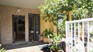 Une terrasse avec un sol carrelé, une plante en pot et un portail blanc.