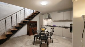 Une cuisine moderne avec des meubles blancs, un escalier noir et une table à manger avec des chaises.