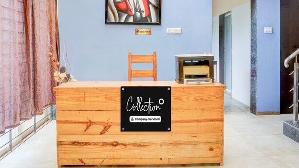 Un comptoir d’accueil avec un panneau indiquant qu’il s’agit d’un point de collecte géré par l’entreprise, une chaise en bois, un tableau abstrait encadré et un escalier menant à un autre espace.