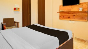 Une chambre d’hôtel avec un lit, un téléviseur fixé sur un panneau en bois, une chaise et une petite table avec une lampe.