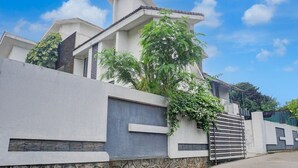 Une maison moderne à deux étages, avec des fondations en pierre, un mur gris et un portail en métal.