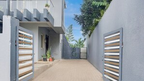 Un bâtiment moderne doté d’une cour dallée, de portails en métal et de plantes en pot.