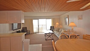 Et værelse med træloft, spisebord med stole, sofa, fjernsyn og balkon med udsigt.