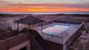 En træterrasse med pool og liggestole, med udsigt over en strand ved solnedgang.