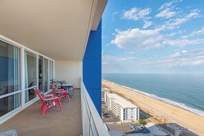 Un balcone con vista sulla spiaggia, un edificio sullo sfondo e cielo sereno.