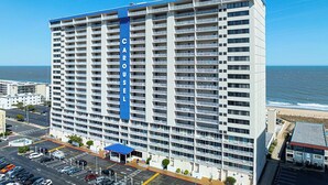 Ett högt hotell med flera balkonger, en framträdande blå vertikal skylt och utsikt över havet.