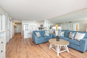 Ein modernes Wohnzimmer mit einem blauen Sofa, einem runden Couchtisch und einer Küche im Hintergrund.