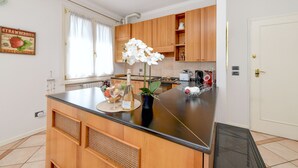 Una cucina con mobili in legno, un piano di lavoro nero, un'orchidea in vaso e una bottiglia di vino.