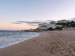 A beach with footprints, a building with multiple stories, and a rocky coastline. - Charming sea view apartment in Platja d'Aro (Platja d'Aro)