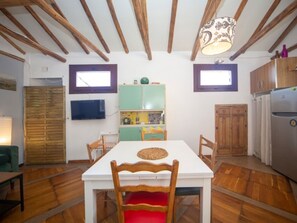 A dining area with a white table, wooden chairs, a ceiling with exposed beams, a green cabinet, a television on the wall, and a refrigerator. - Stunning duplex in Granada, Albaicín view - 4 guests (Granada)