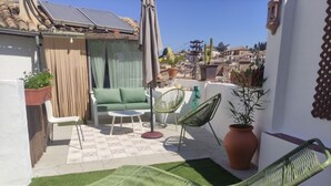 A patio with a green chair, a sofa, and a small table. There are potted plants and a view of the city.