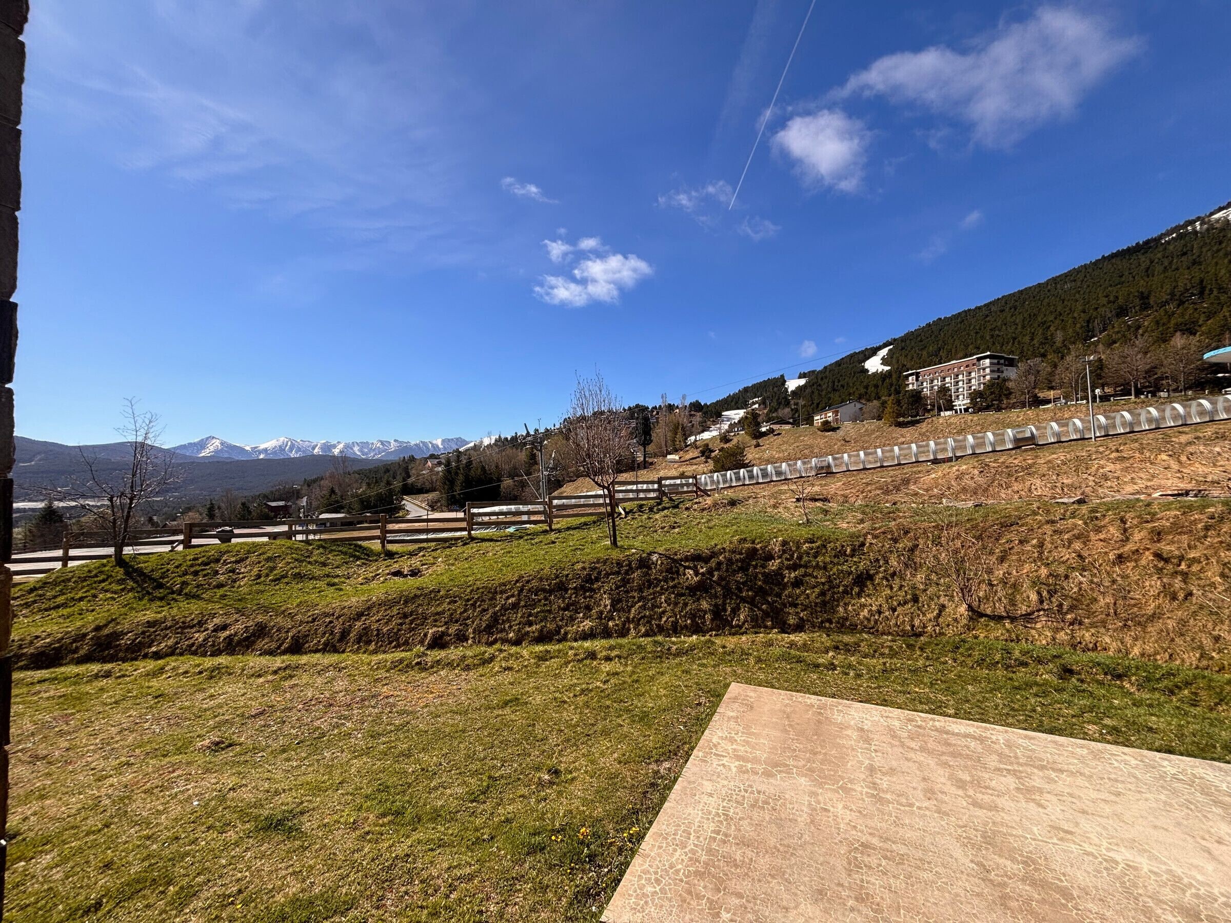 Un paysage montagneux sous un ciel dégagé, avec une zone pavée au premier plan et une vue lointaine sur des montagnes enneigées.