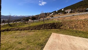 Bjergrigt landskab med klar himmel, en asfalteret plads i forgrunden og fjerne, sneklædte bjerge.