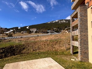 A residential building with stone facade balconies, a concrete patio, and a view of a hilly landscape with a ski slope in the background. - Convenient apartment, slope view - 6 guests (Les Angles)