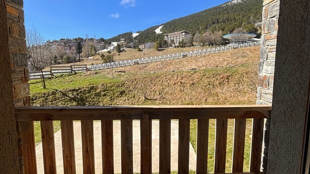En bygning i sten med en træbalkon, der giver udsigt over et bakket landskab med sparsom vegetation og enkelte bygninger i det fjerne.