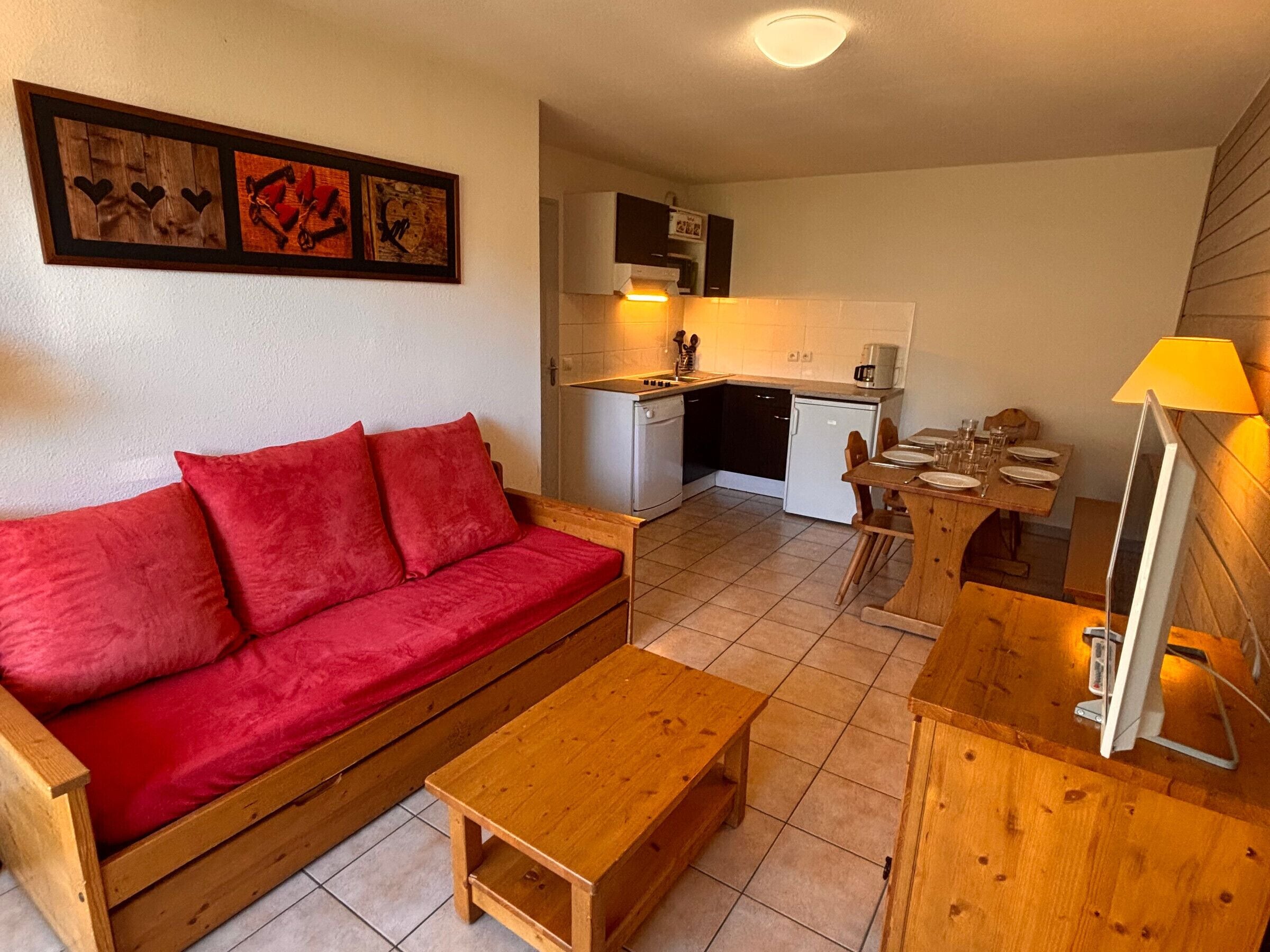 Un espace de vie compact comprenant un canapé rouge, des meubles en bois, une kitchenette et un coin repas.