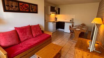 Un espace de vie compact comprenant un canapé rouge, des meubles en bois, une kitchenette et un coin repas.