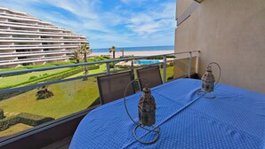 Un balcon avec une table, deux lanternes et une vue sur un hôtel, une plage et une piscine.