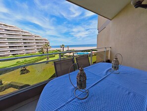 Un balcon avec une table, deux lanternes et une vue sur un hôtel, une plage et une piscine.