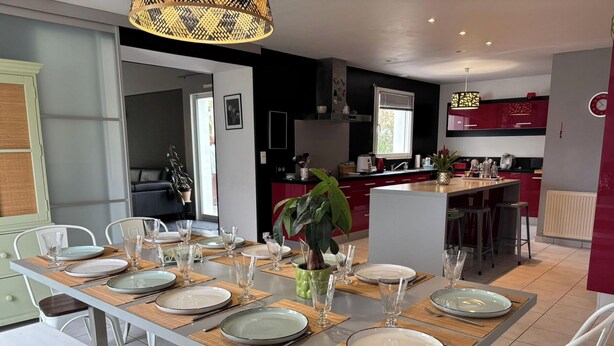 Una cocina moderna con armarios rojos, un comedor con una mesa grande dispuesta para seis personas, y un amplio ventanal que proporciona luz natural.