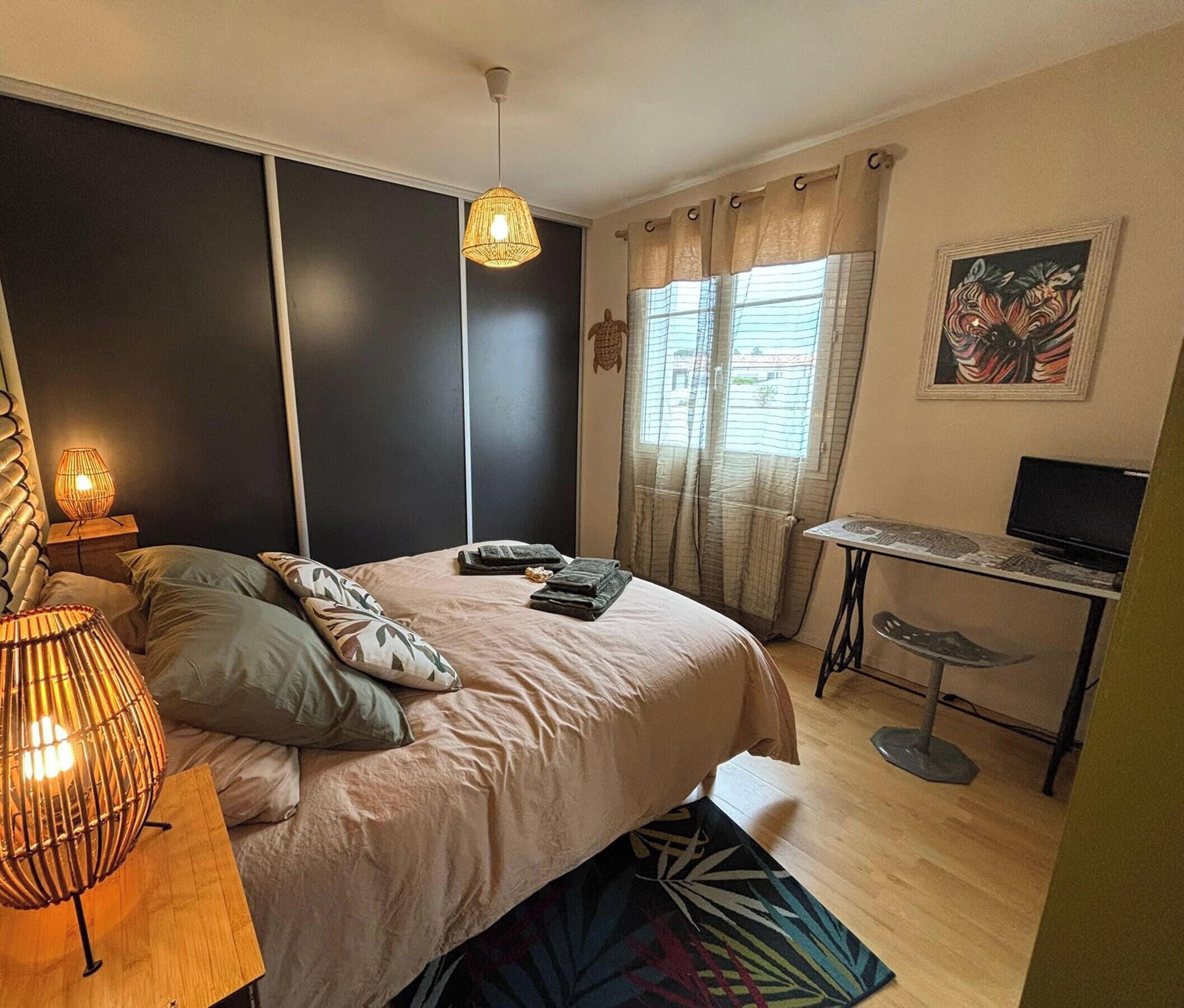 Ein Schlafzimmer mit einem Bett, Nachttischlampen, einem Schreibtisch mit Computer und einem Fenster mit Vorhängen.
