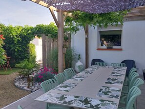 A covered patio with a table and chairs, surrounded by greenery and a wooden fence. - Spacious house near beaches - 12 guests (Challans)