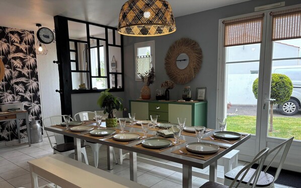 A dining area with a table set for four, a clock, and a view of the outside.