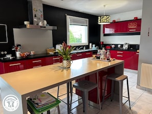 A modern kitchen with red cabinets, a central island, and a window providing natural light.