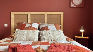 Una cama con cabecera de madera, varios cojines y dos toallas rojas sobre la cama.