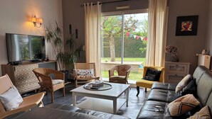 Una sala de estar con televisor, sillas de mimbre, sofá de cuero y vista a un jardín.