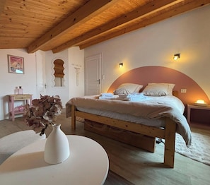 A bedroom with a wooden bed, a white round table, a vase with dried flowers, and a wall-mounted light fixture. - Spacious house near beaches - 12 guests (Challans)