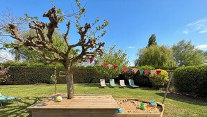 Un jardín con una zona de juegos de madera, un árbol y un banderín decorativo.