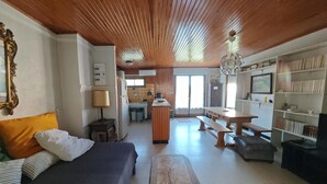 Una stanza con soffitto in legno, un letto, una scrivania, una panca, una libreria e un angolo cottura.