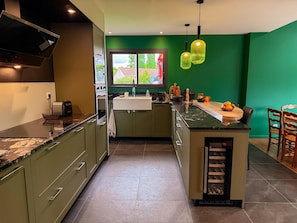Une cuisine moderne avec des meubles de couleur verte, un plan de travail en marbre, un four encastré, un évier et une fenêtre donnant sur un paysage verdoyant.