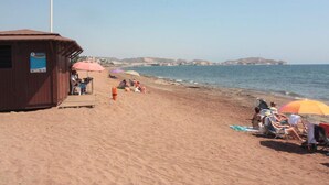 Ein Strand mit einem Holzgebäude, Liegestühlen und Sonnenschirmen.