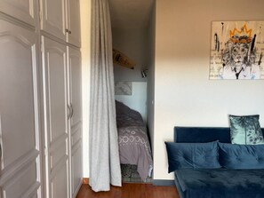 A bedroom with a bed, a wardrobe, a curtain, a blue sofa, and a wall art piece. - Canet Plage: Cozy studio with terrace and wifi, perfect for 2 (Canet-en-Roussillon)