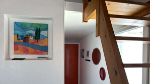 A hallway with a colorful painting, a red door, and a wooden staircase. - House with parking - 4 guests (Bretignolles-sur-Mer)