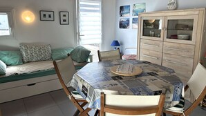 A cozy room with a bed, a dining table with a quilt, a cabinet with glass doors, and a window with blinds. - House with parking - 4 guests (Bretignolles-sur-Mer)