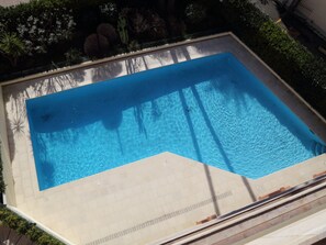 A rectangular swimming pool with clear blue water, surrounded by a tiled deck and bordered by greenery. - Studio with terrace - sea view, pool (Menton)