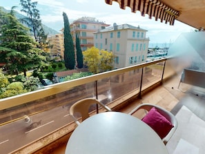 A balcony with a view of a road, buildings, and trees. - Studio with terrace - sea view, pool (Menton)